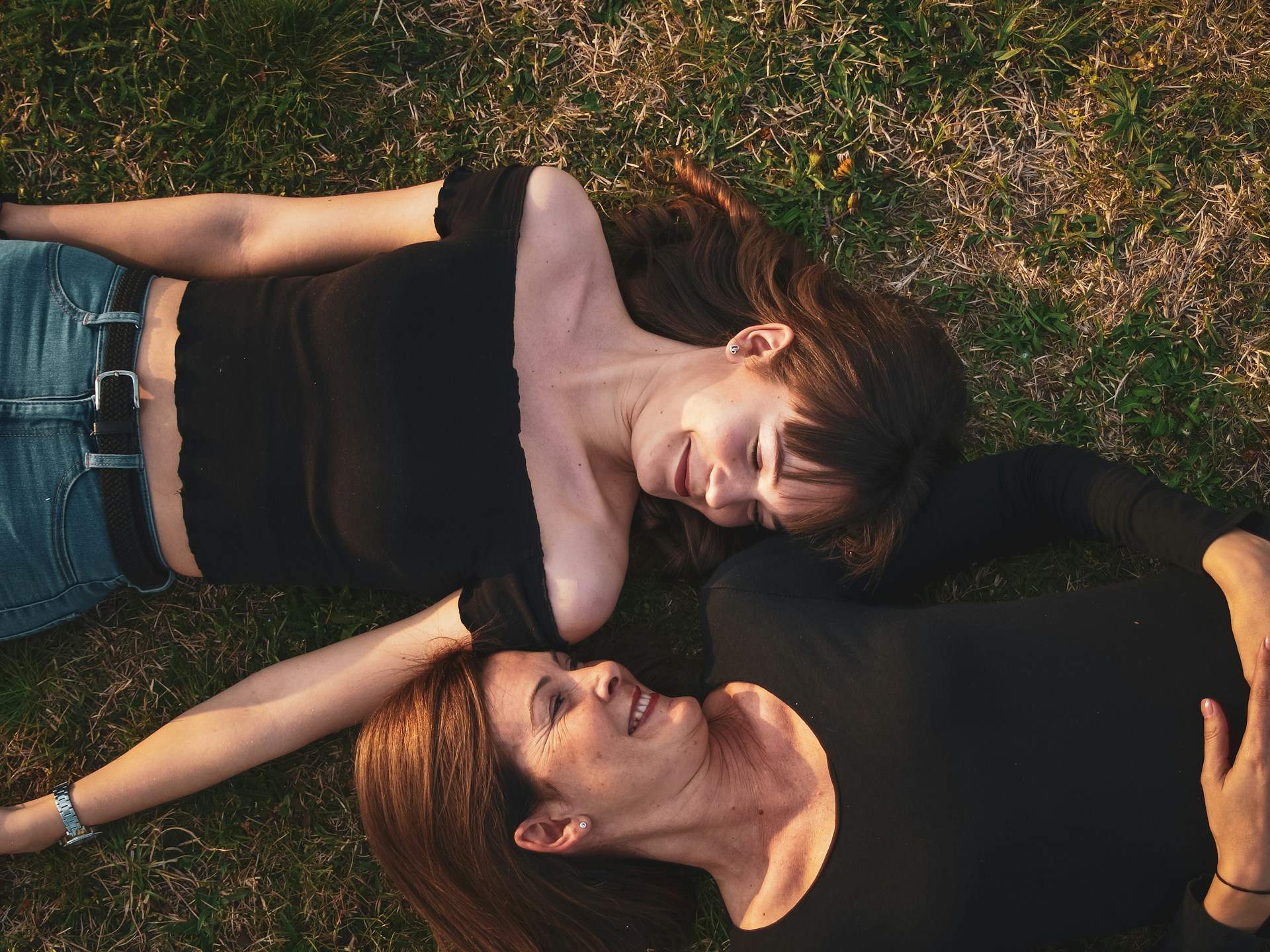 Two women lying on the grass nurture their bond as they show love and enjoying a peaceful moment together.