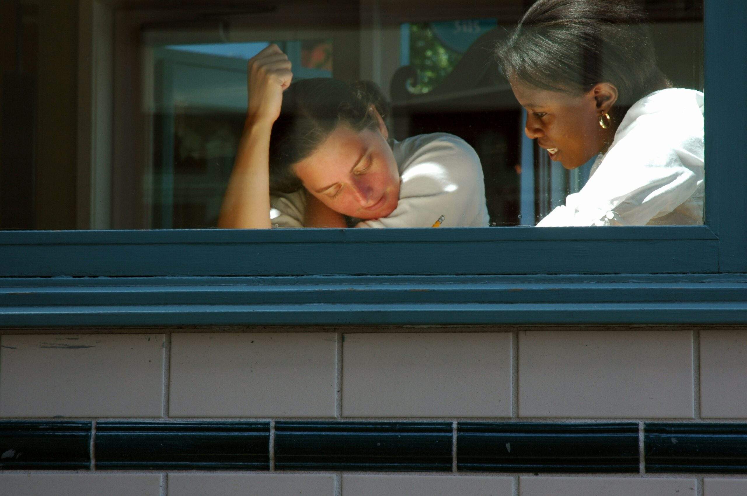 Two women sit by a window, leaning in and talking closely, as sunlight highlights a moment of leadership mindset between them.