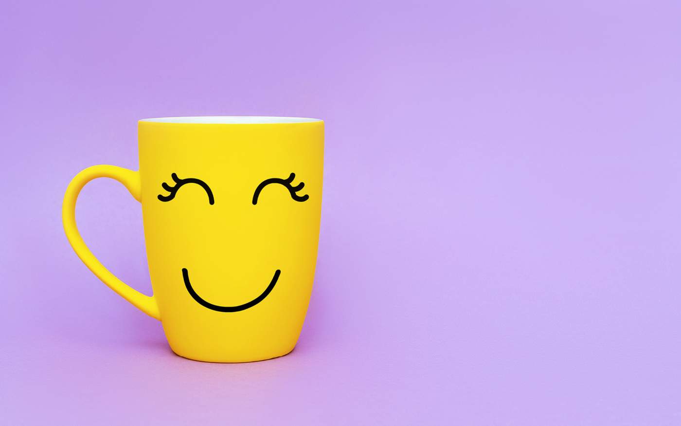 A yellow mug with a happy smiling face on a purple background.